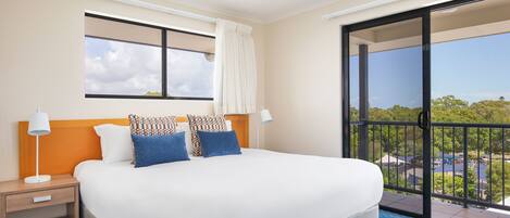 Ein Hotelzimmer mit einem großen Bett, einem Nachttisch, einem Fenster mit Blick und einem Balkon mit Geländer.