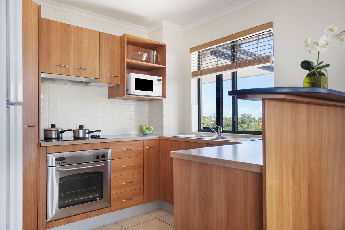 Une cuisine moderne avec des meubles en bois, un four à micro-ondes encastré, un four traditionnel et une fenêtre avec des stores.
