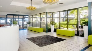 Un área de recepción moderna con un mostrador curvo, asientos de color verde brillante, ventanas amplias y plantas en macetas.