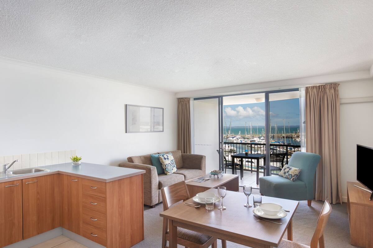 Un salon moderne comprenant une cuisine, un coin repas et un balcon avec vue sur le port de plaisance.