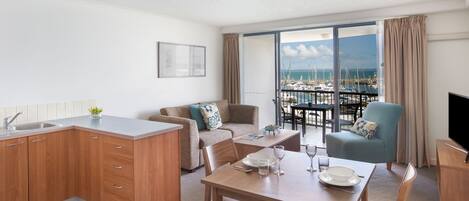 A modern living room with a kitchen, dining area, and a balcony with a view of the marina.