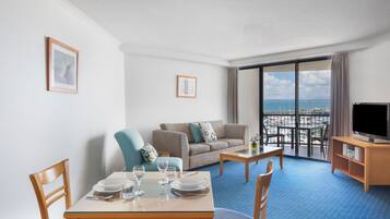 A hotel room with a dining area, a sofa, a TV, and a balcony with a view.