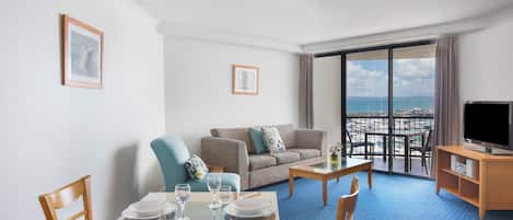 A hotel room with a dining area, a sofa, a TV, and a balcony with a view.