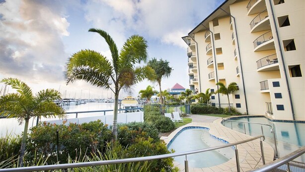 Un hotel con piscina, palmeras y un puerto deportivo al fondo.