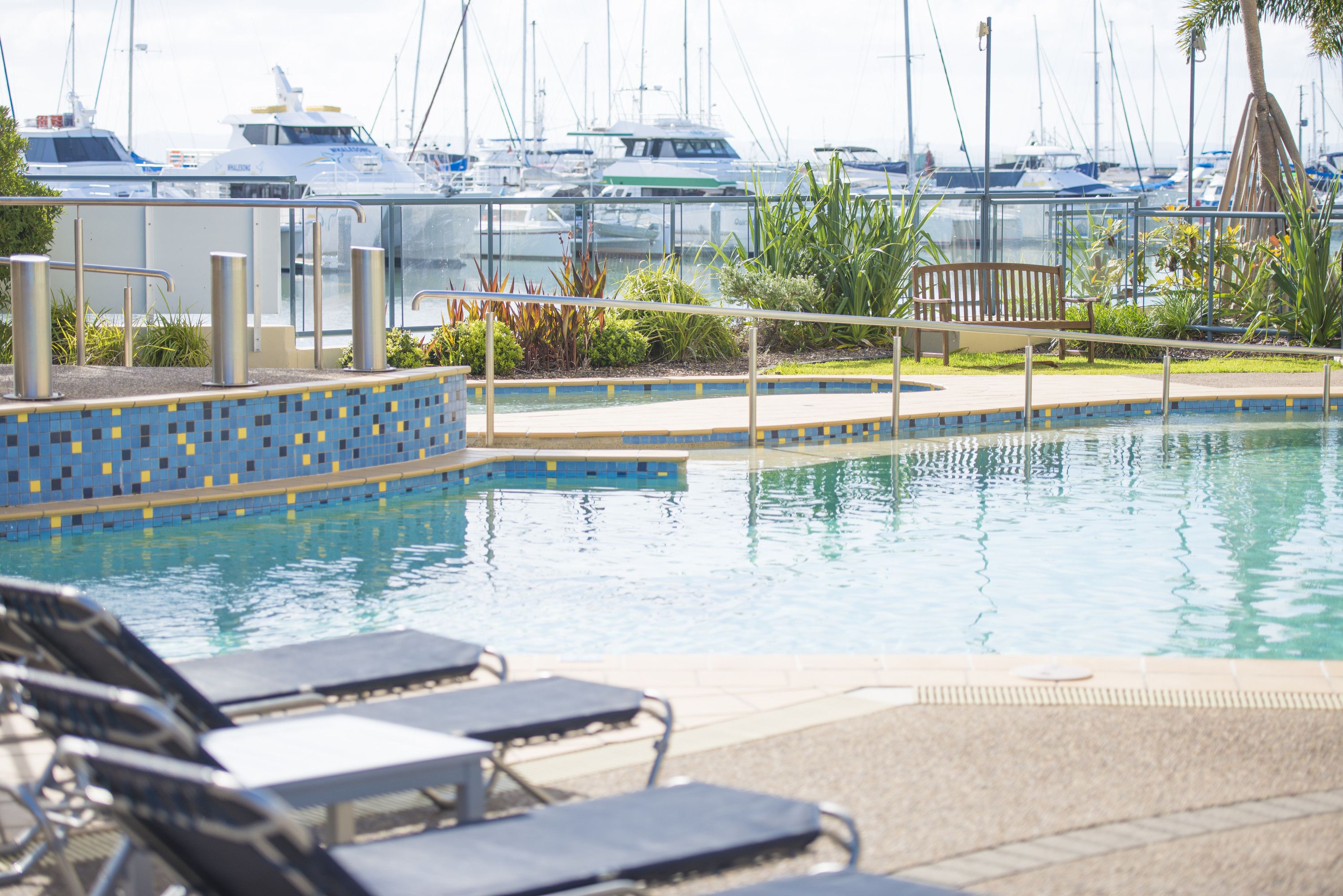 A pool area with lounge chairs, a small garden, and a view of boats in the background.