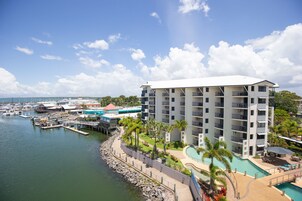 Un hotel de varios pisos con piscina, situado cerca de un puerto deportivo con barcos.