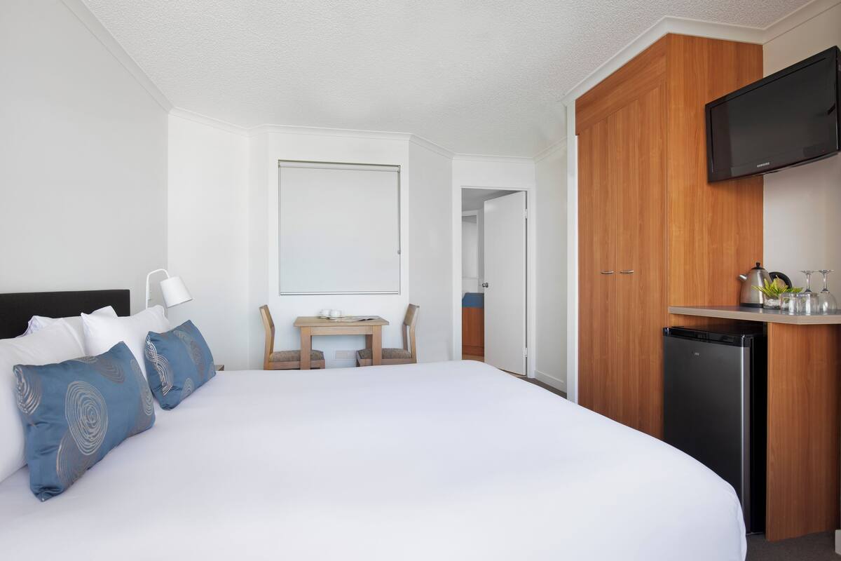 Une chambre d’hôtel avec un grand lit, un bureau, une télévision et un réfrigérateur.