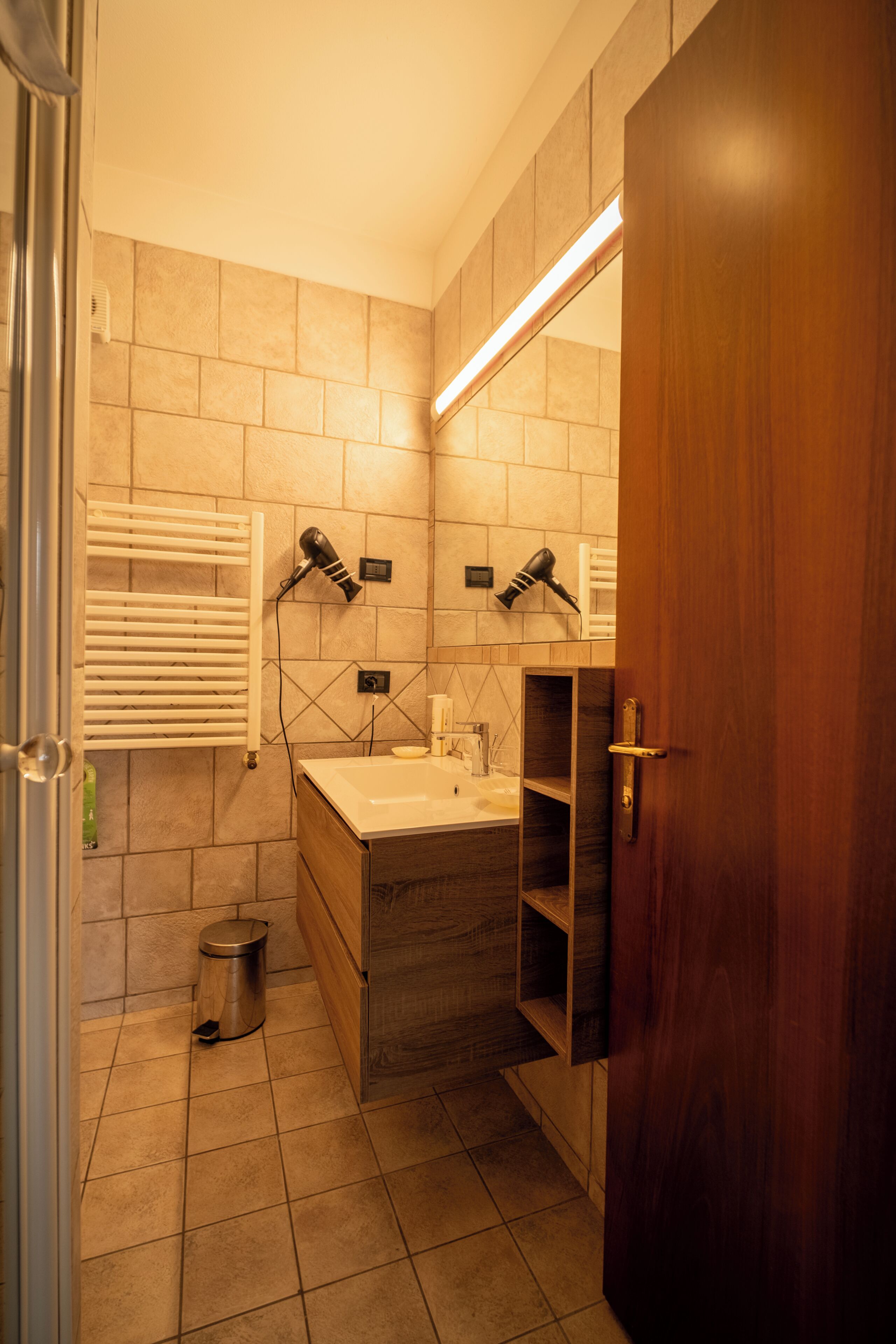 Un baño con tocador de madera, espejo, toallero y cubo de basura.