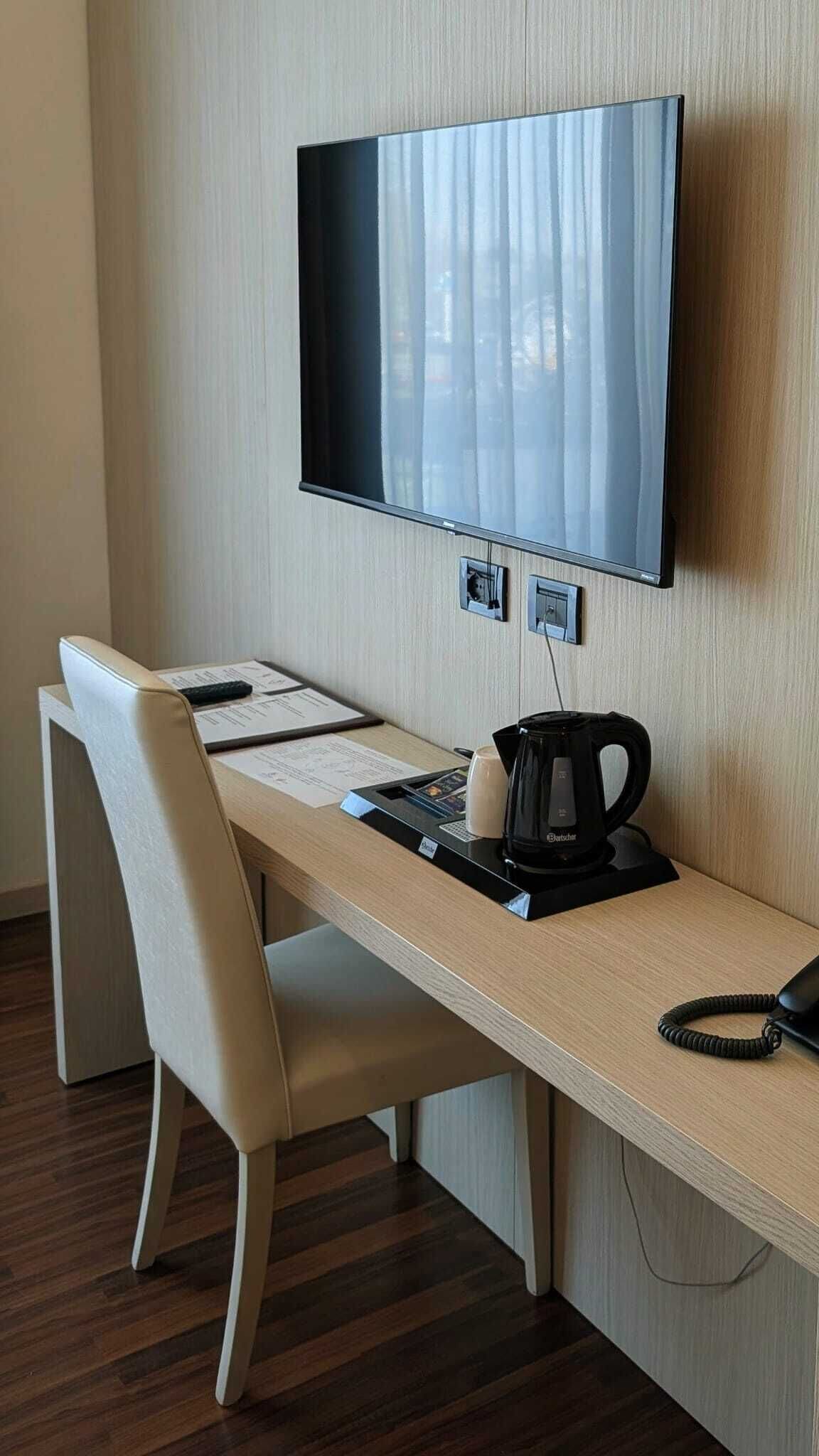 Ein Hotelzimmer mit Schreibtisch, Stuhl, Flachbildfernseher, Kaffeemaschine und Telefon.
