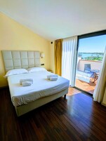 A hotel room with a large bed, a view of the outdoors through a sliding glass door, and a balcony with outdoor furniture.