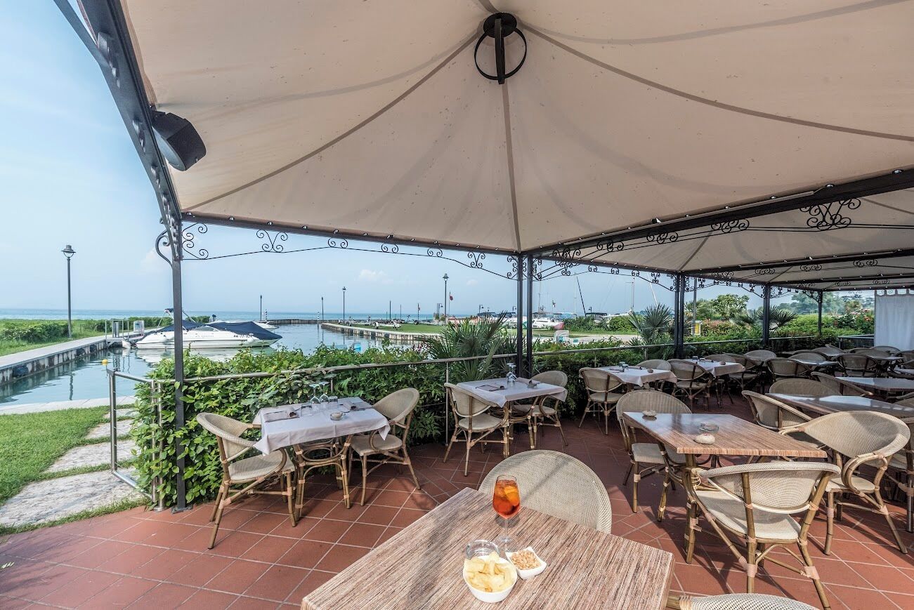 Un patio al aire libre con mesas y sillas, con vista a un puerto deportivo y un canal.
