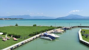 Un port de plaisance avec des bateaux amarrés, une zone herbeuse avec des chaises longues et une vue dégagée sur les montagnes lointaines.