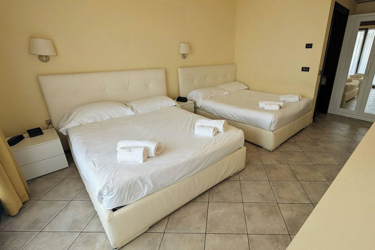 A hotel room with two beds, a nightstand, a lamp, and a bathroom visible through an open door.