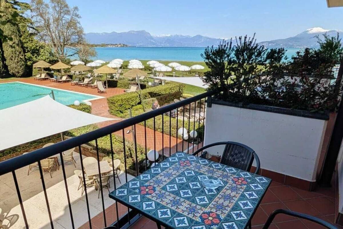 A balcony with a view of a swimming pool, lounge chairs, and a table with a patterned tablecloth.