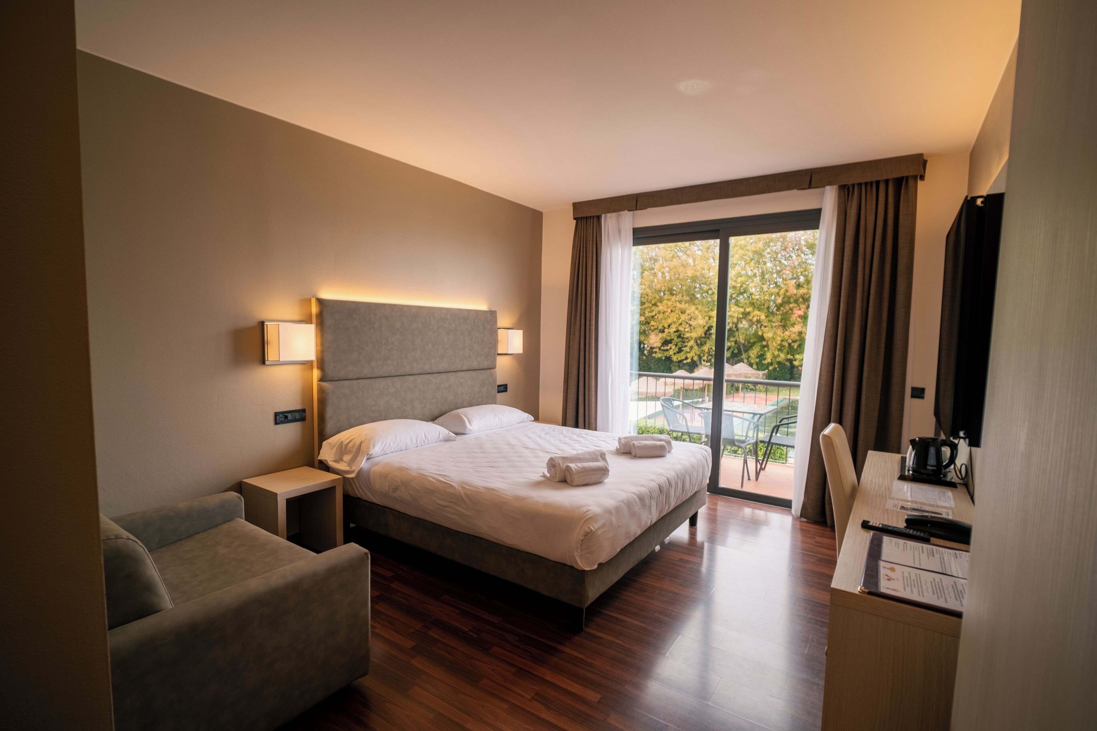 Habitación de hotel con cama, escritorio, silla, mesita de noche y vistas al exterior.