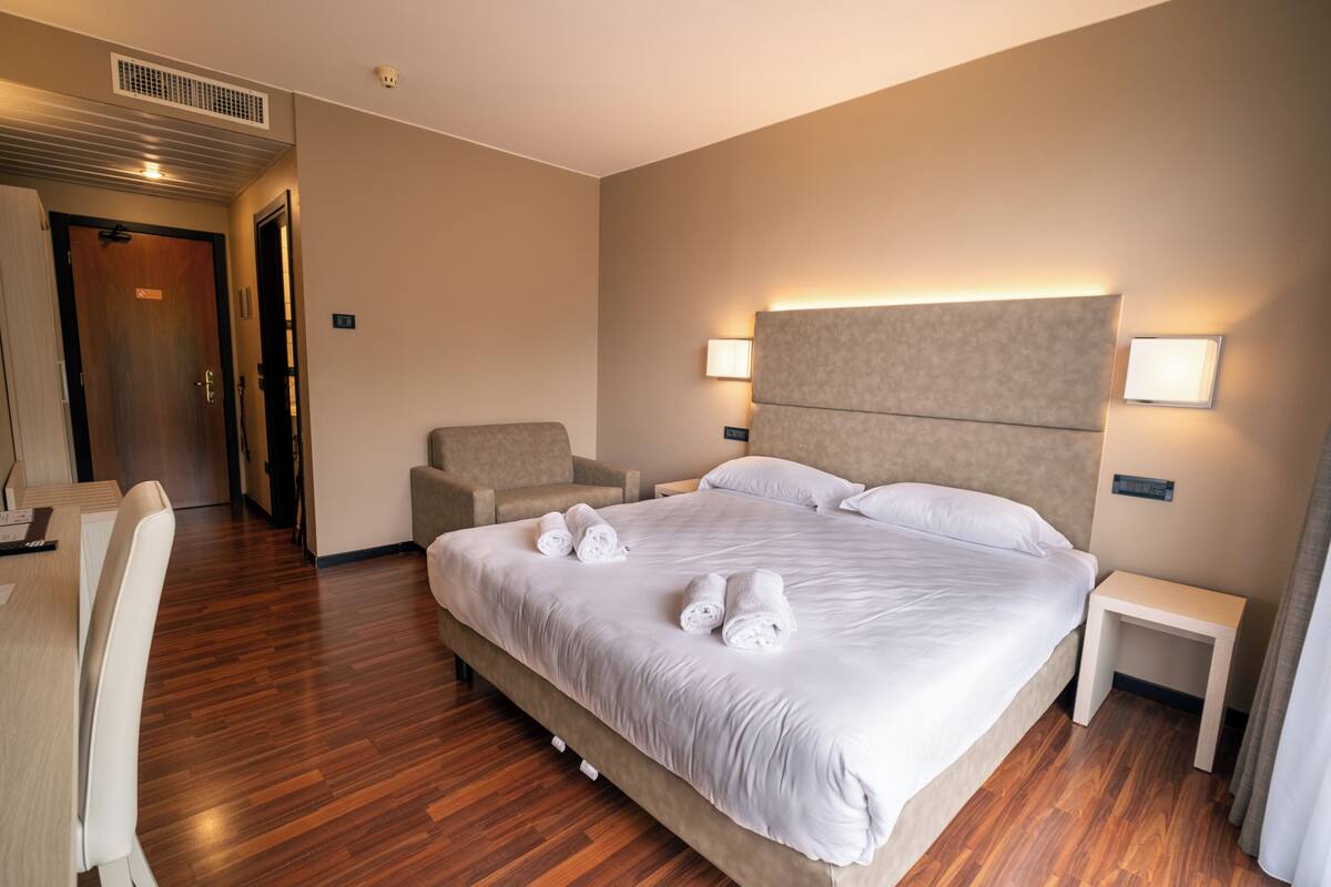 A hotel room with a large bed, two bedside tables, a chair, and a desk.