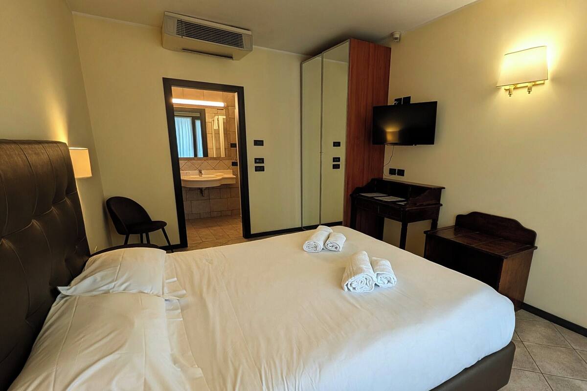 A hotel room with a bed, a desk, a chair, a television, and a mirror.