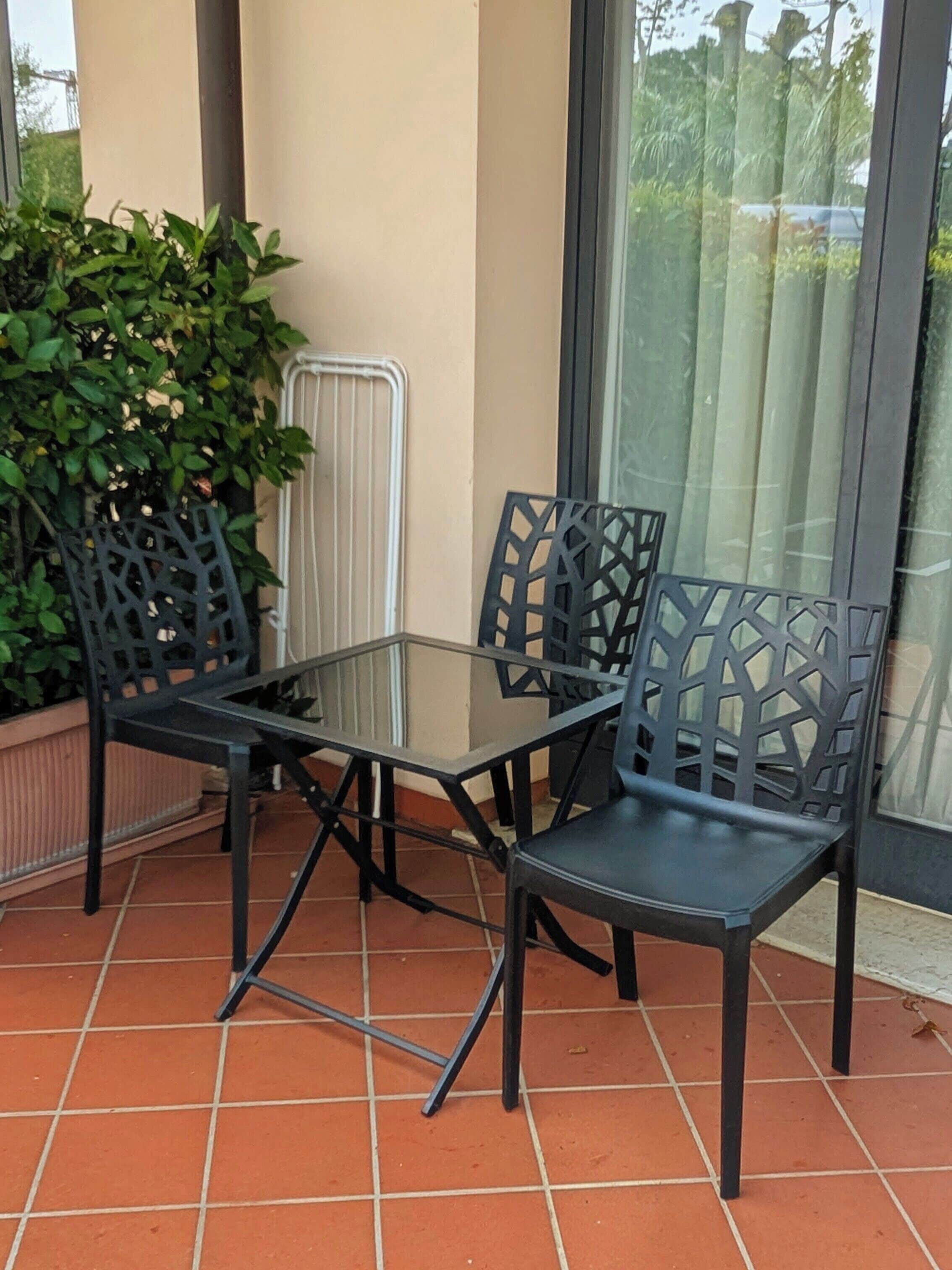 A glass-top table with four chairs, a potted plant, and a radiator on a tiled patio.
