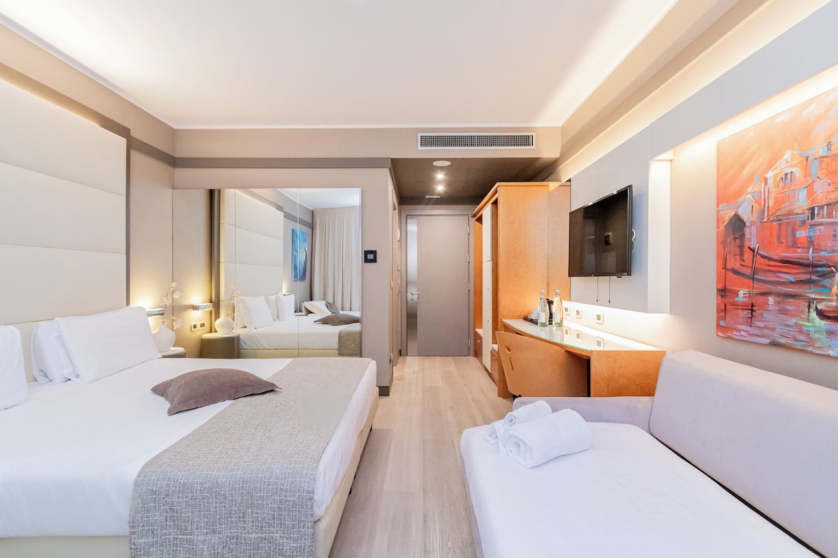 A hotel room with two beds, a sitting area, a TV, and a painting on the wall.