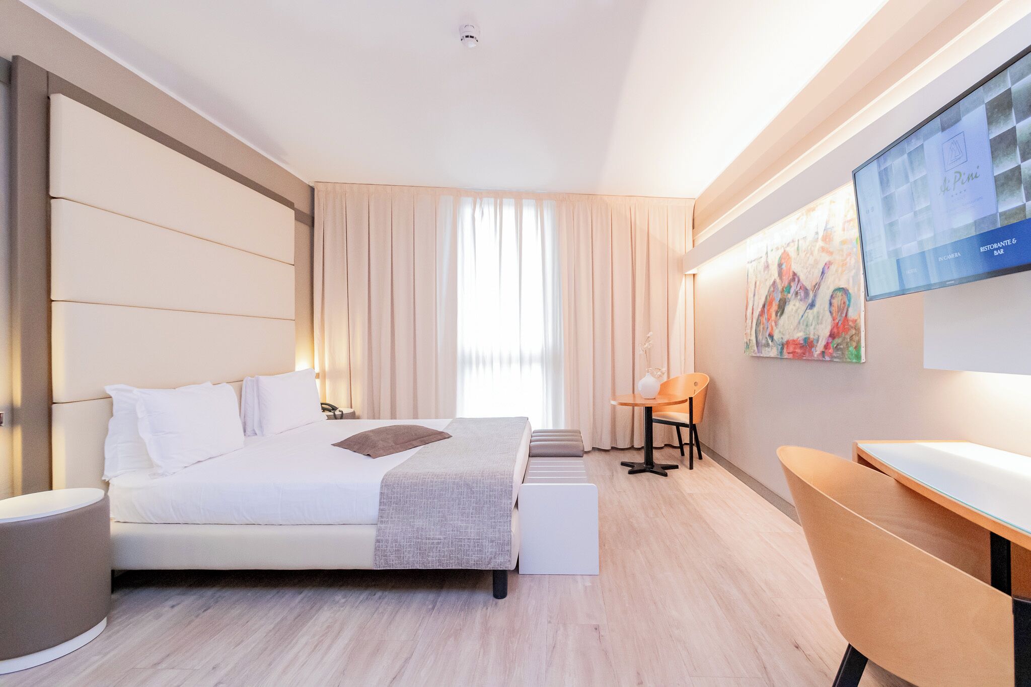 A modern hotel room with a large bed, a desk, and a television on the wall.