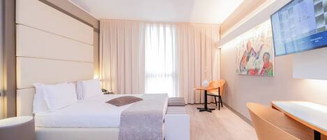 A modern hotel room with a large bed, a desk, and a television on the wall.