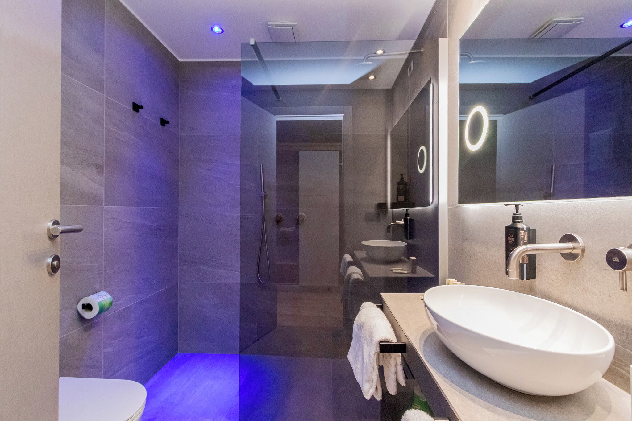 Un baño moderno con un espejo grande, un lavamanos blanco y una zona de ducha.