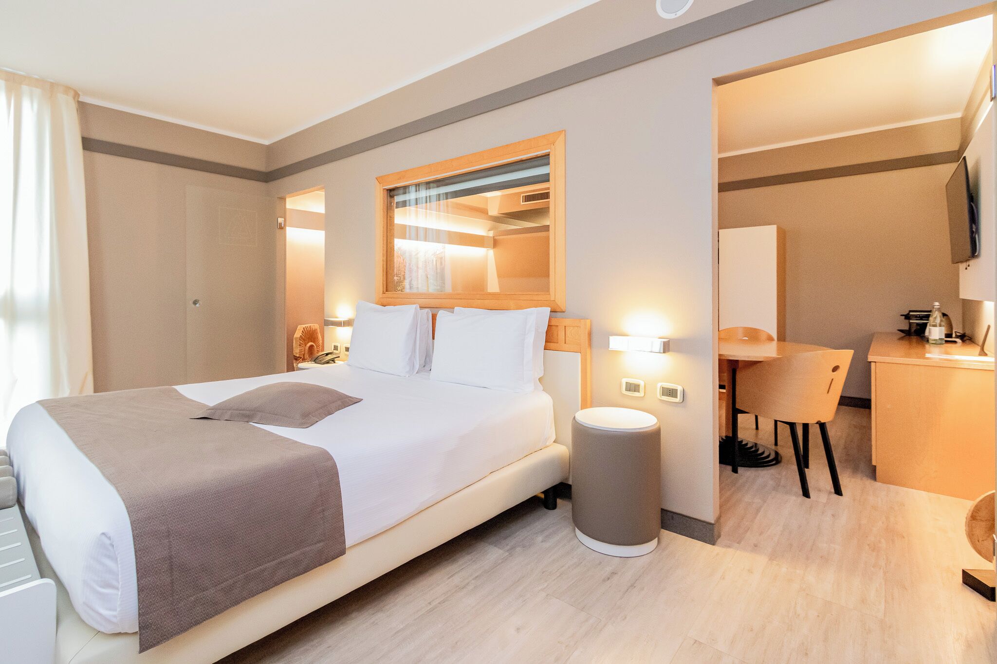 Ein Hotelzimmer mit Bett, Nachttisch, Lampe, Stuhl, Schreibtisch und Spiegel.