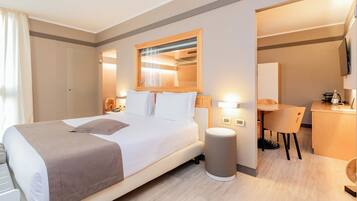 Ein Hotelzimmer mit Bett, Nachttisch, Lampe, Stuhl, Schreibtisch und Spiegel.