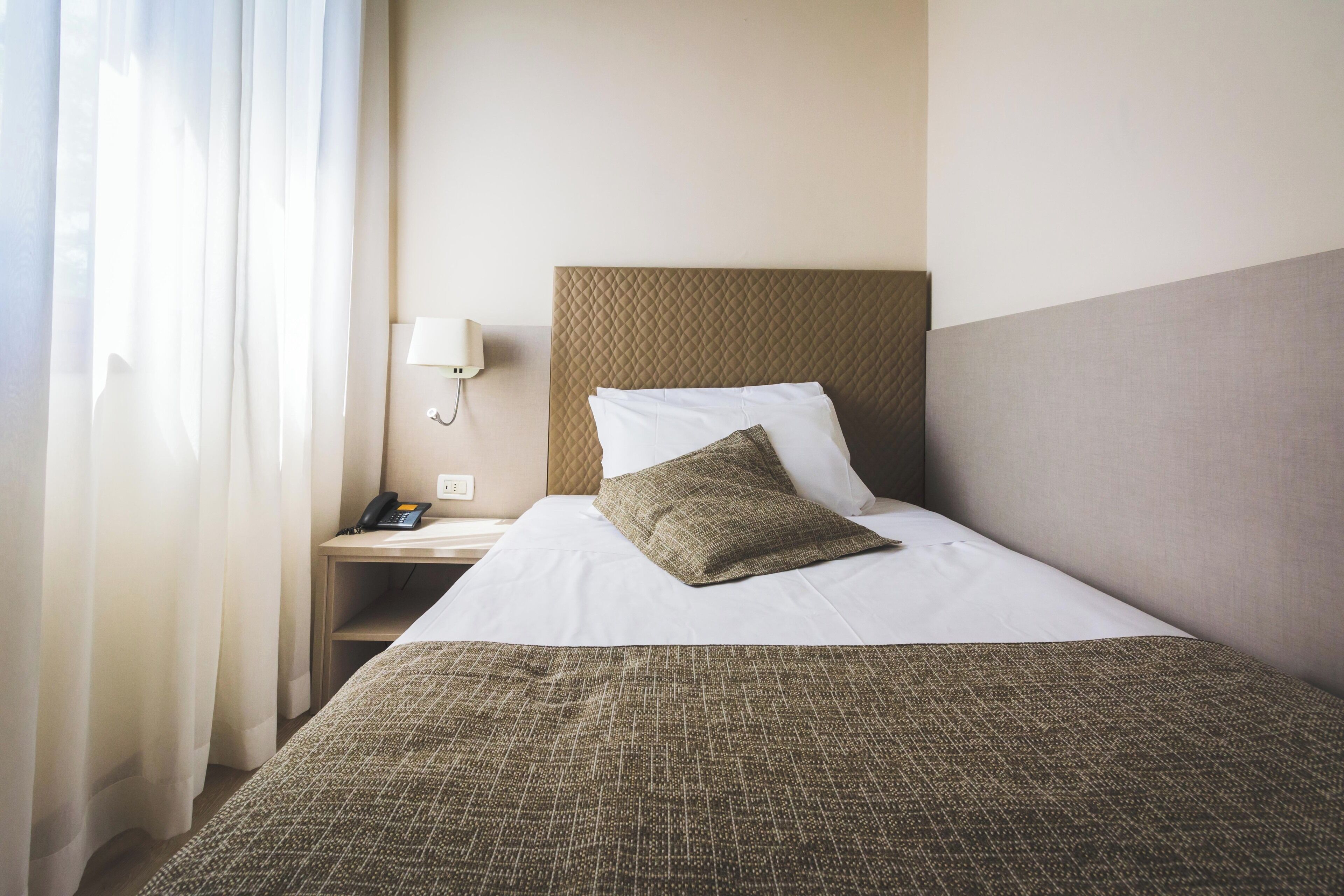 Et hotelværelse med en seng, et sengebord med lampe og en telefon.