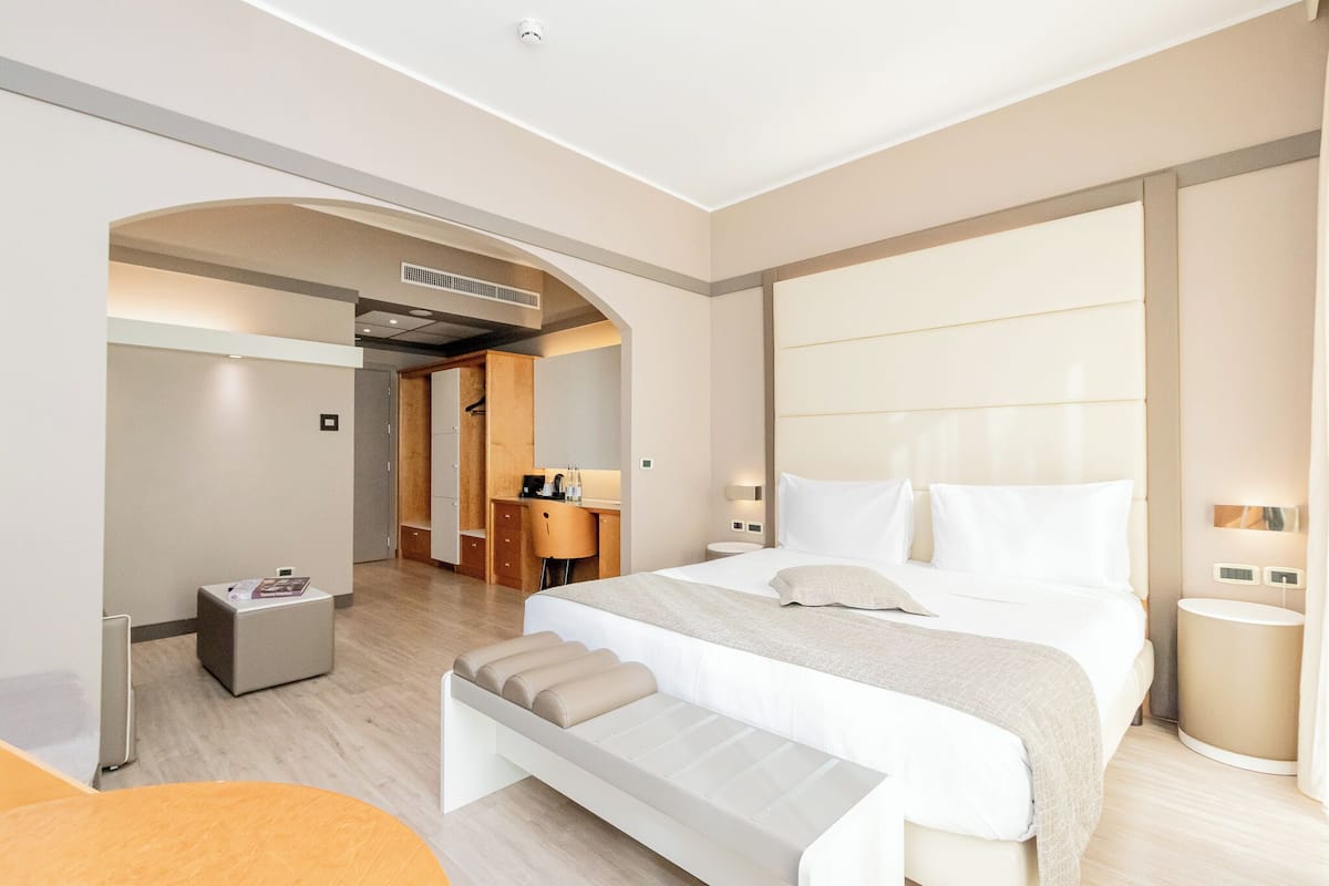 A modern hotel room with a large bed, a desk, and a seating area.