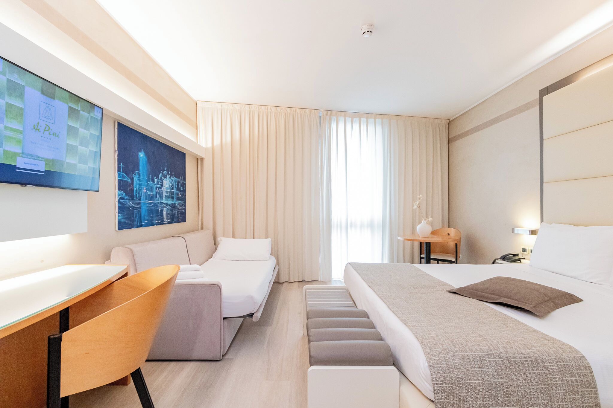 A modern hotel room with a bed, a desk, a chair, and a TV.