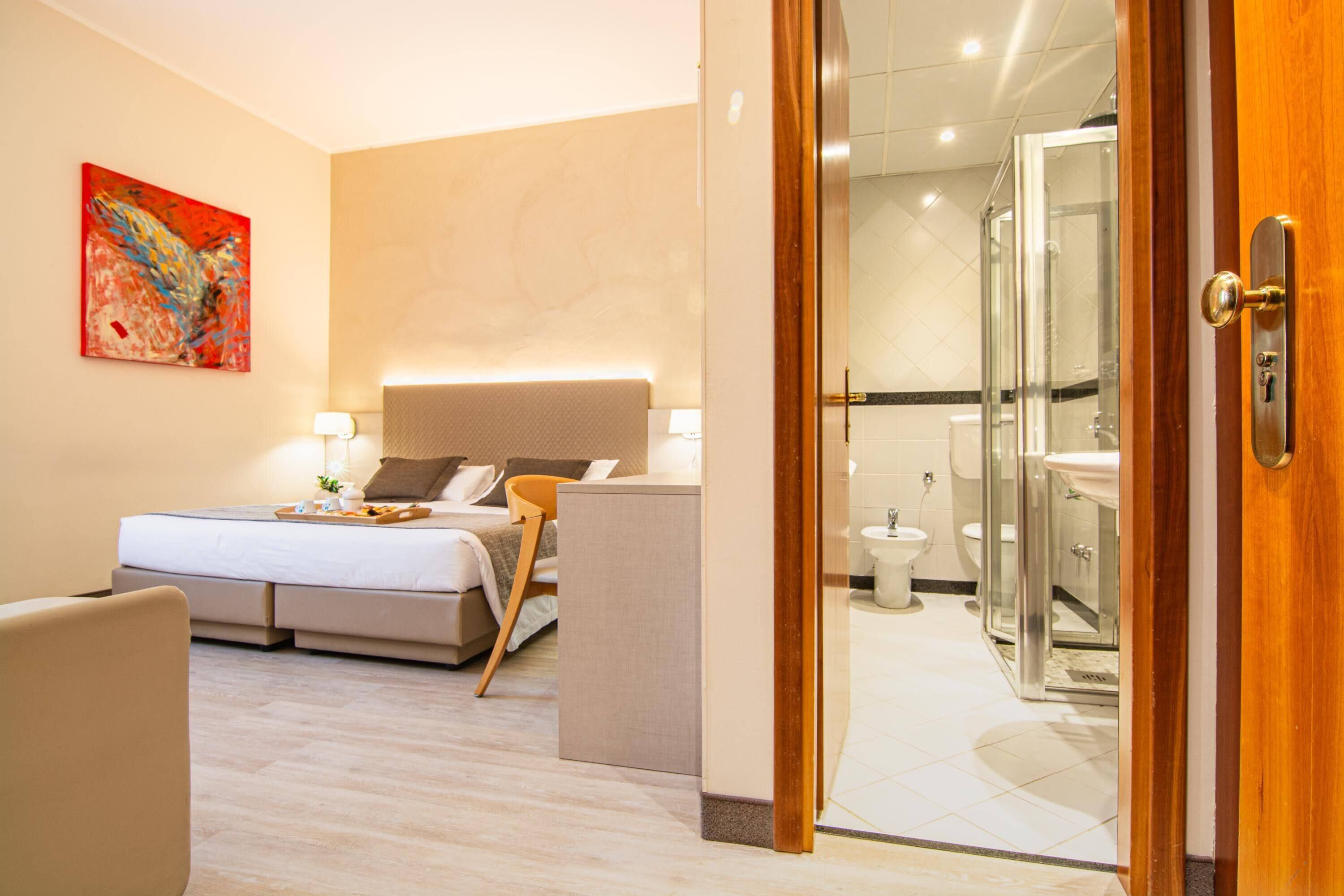 Una habitación de hotel moderna con cama, mesita de noche y zona de ducha con paredes de vidrio.