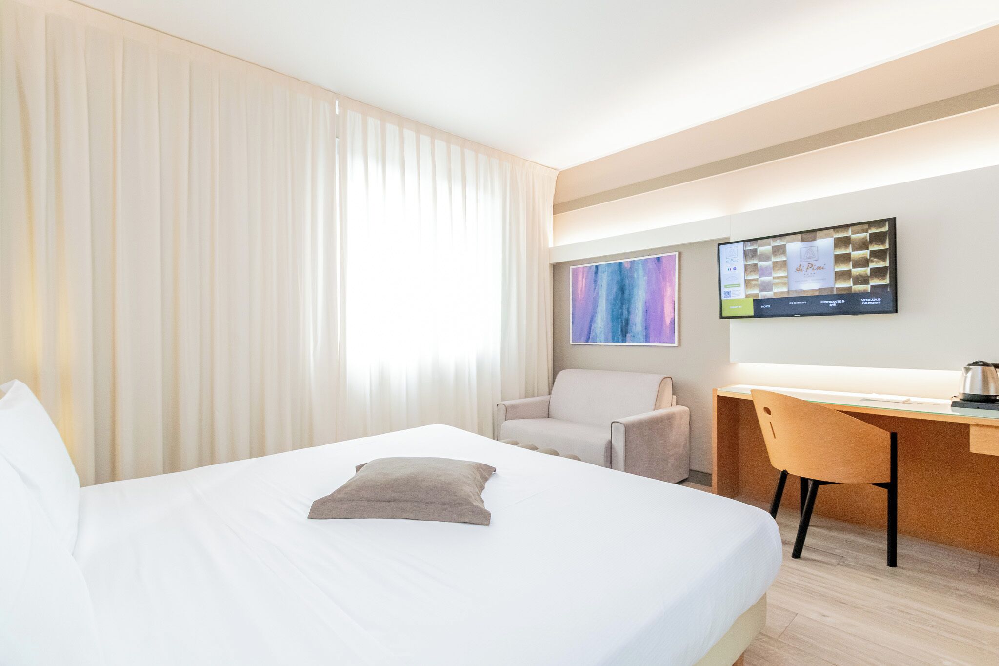 A hotel room with a bed, a desk, a chair, and a television mounted on the wall.