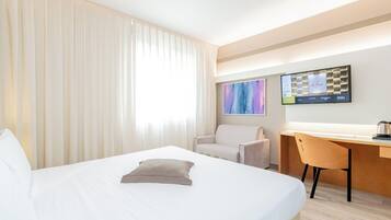 A hotel room with a bed, a desk, a chair, and a television mounted on the wall.