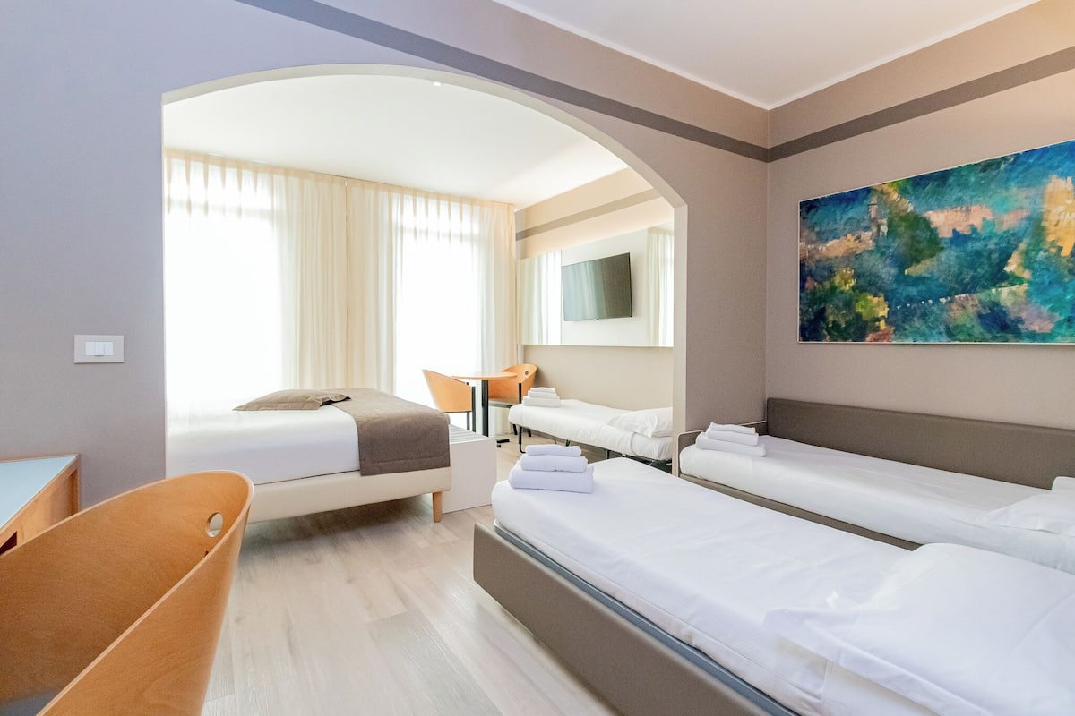 A hotel room with two beds, a desk, a chair, a TV, and a painting on the wall.