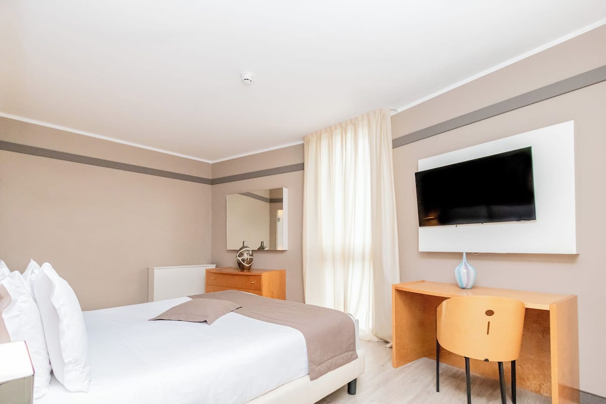 A modern hotel room with a bed, a desk, a TV, and a mirror.