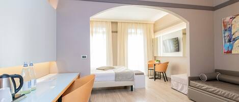 A modern hotel room with a bed, a desk, a chair, a sofa, and a large window with curtains.