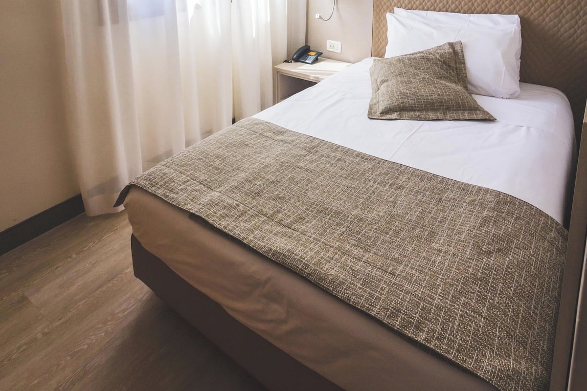 A hotel room with a bed, a nightstand, a lamp, and sheer curtains.