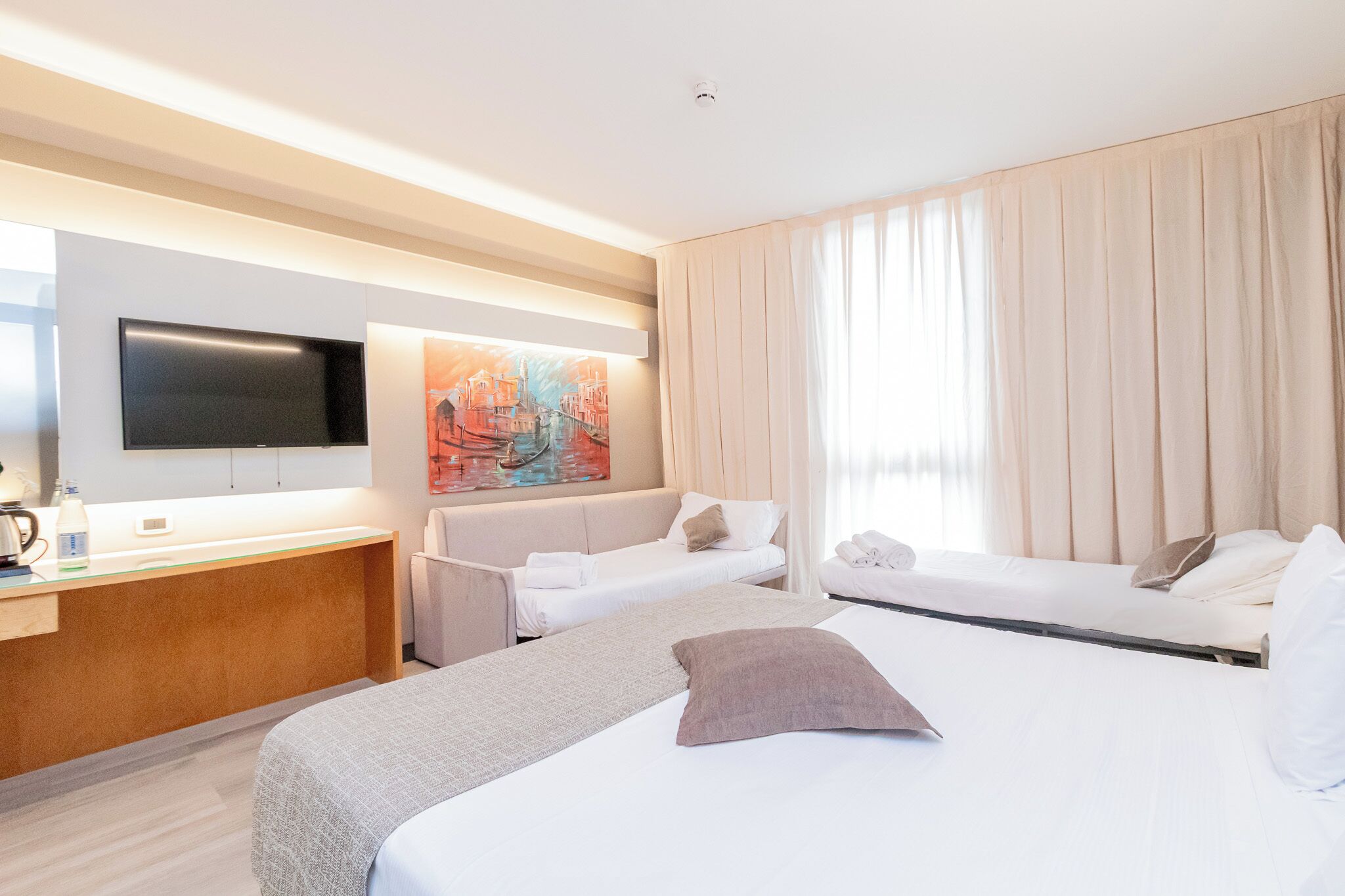 Una habitación de hotel con una cama, un sofá, un escritorio y un televisor de pantalla plana, y un cuadro en la pared.