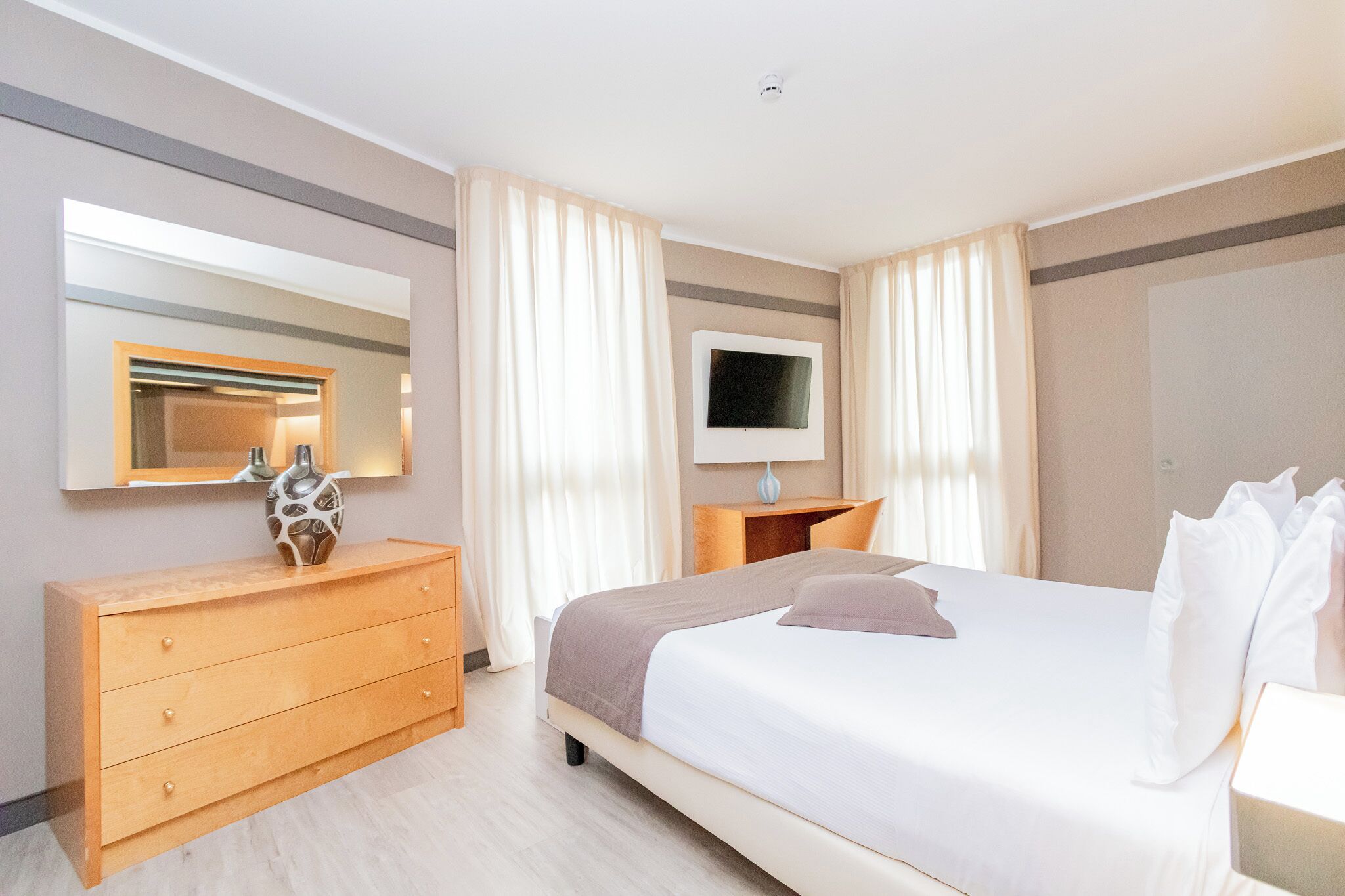 A hotel room with a bed, a wooden dresser, a TV, and a mirror.