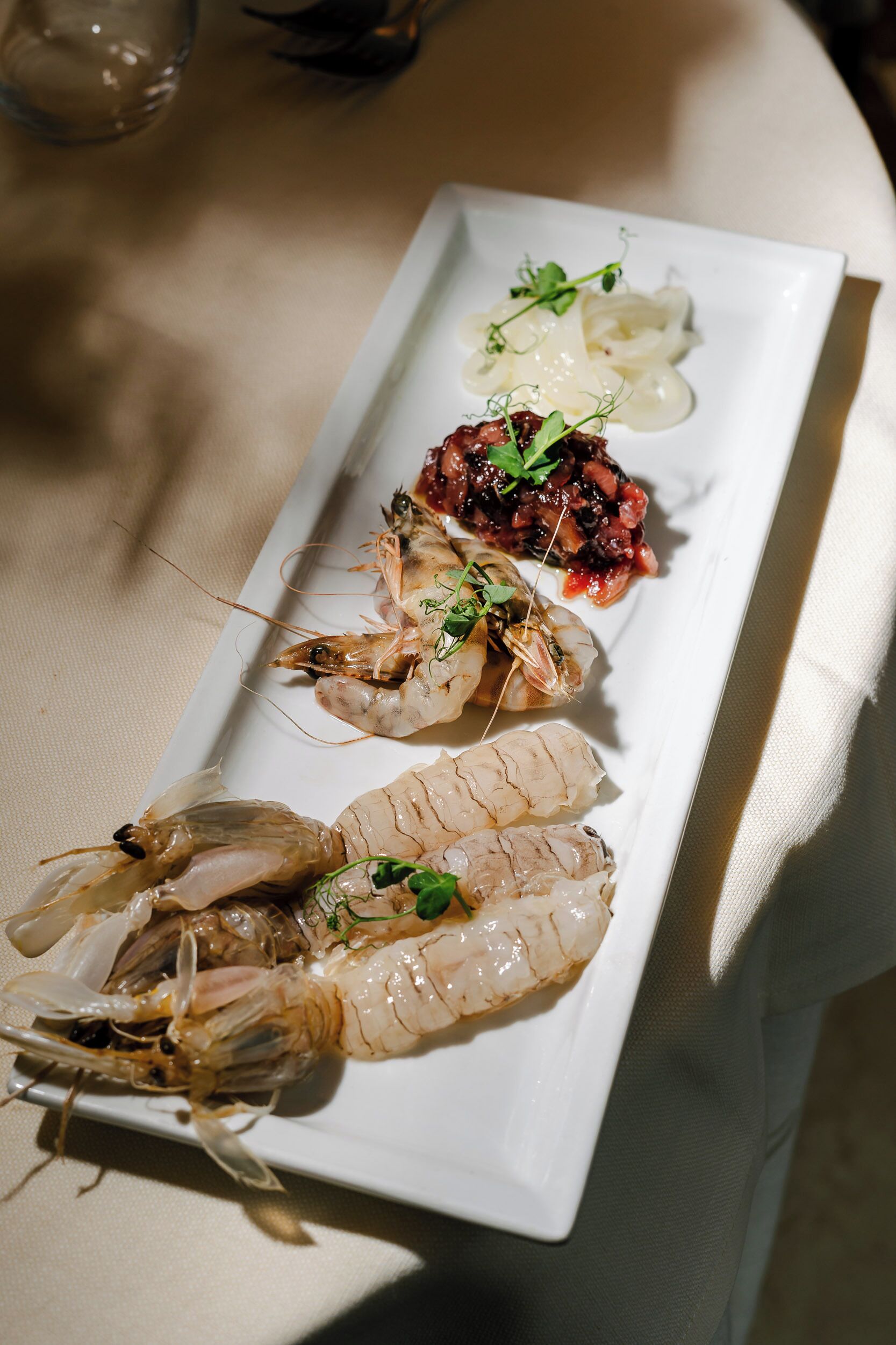 A white rectangular plate with three cooked shrimp and a small portion of a red sauce garnished with herbs.