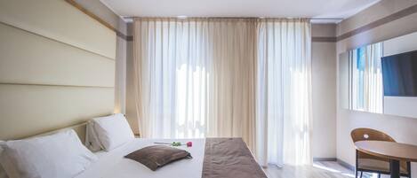 Ein Hotelzimmer mit einem großen Bett, einem Schreibtisch und einem an der Wand befestigten Fernseher.