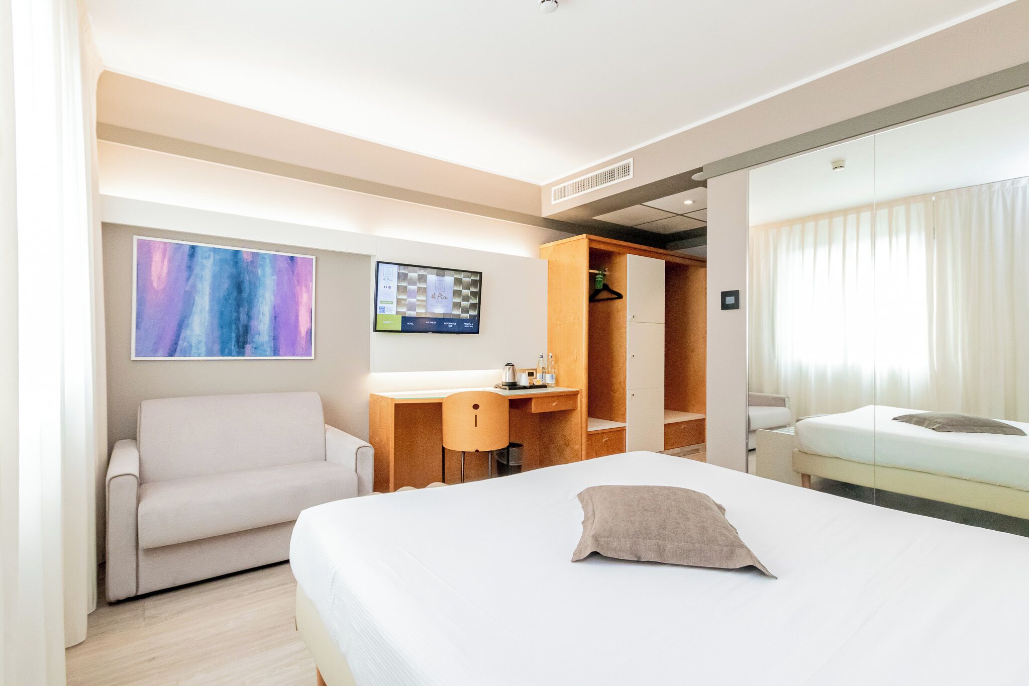 Una habitación de hotel moderna con cama, escritorio, silla, sofá y armario.