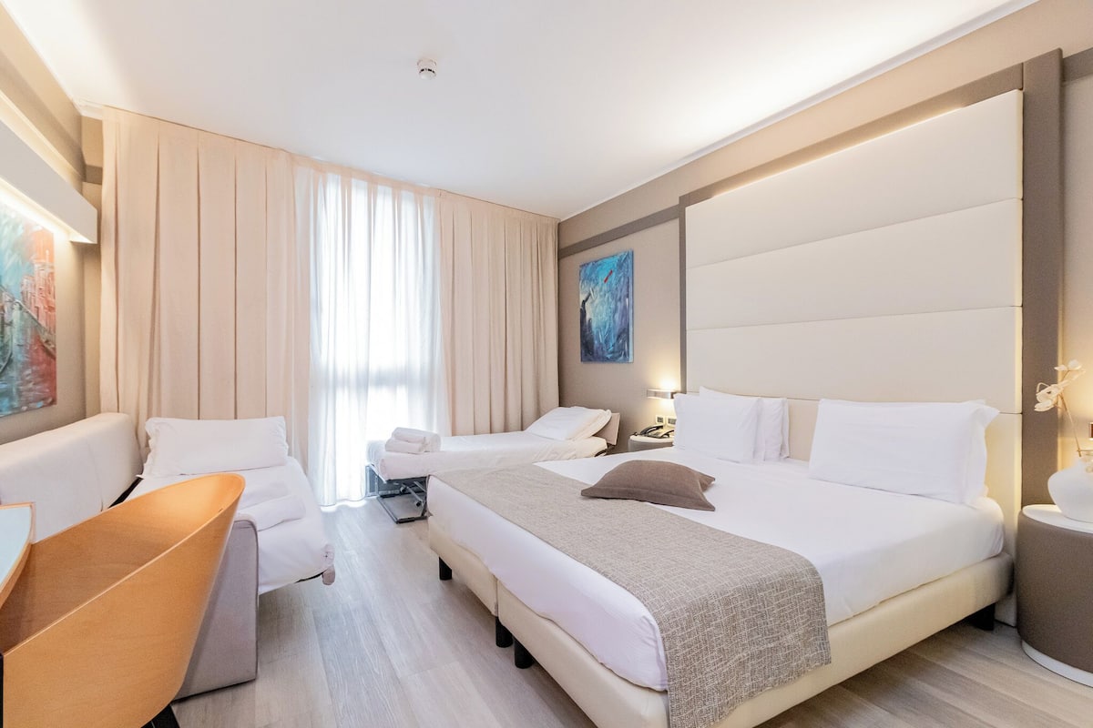 A hotel room with a large bed, a smaller bed, a sofa, and a desk.