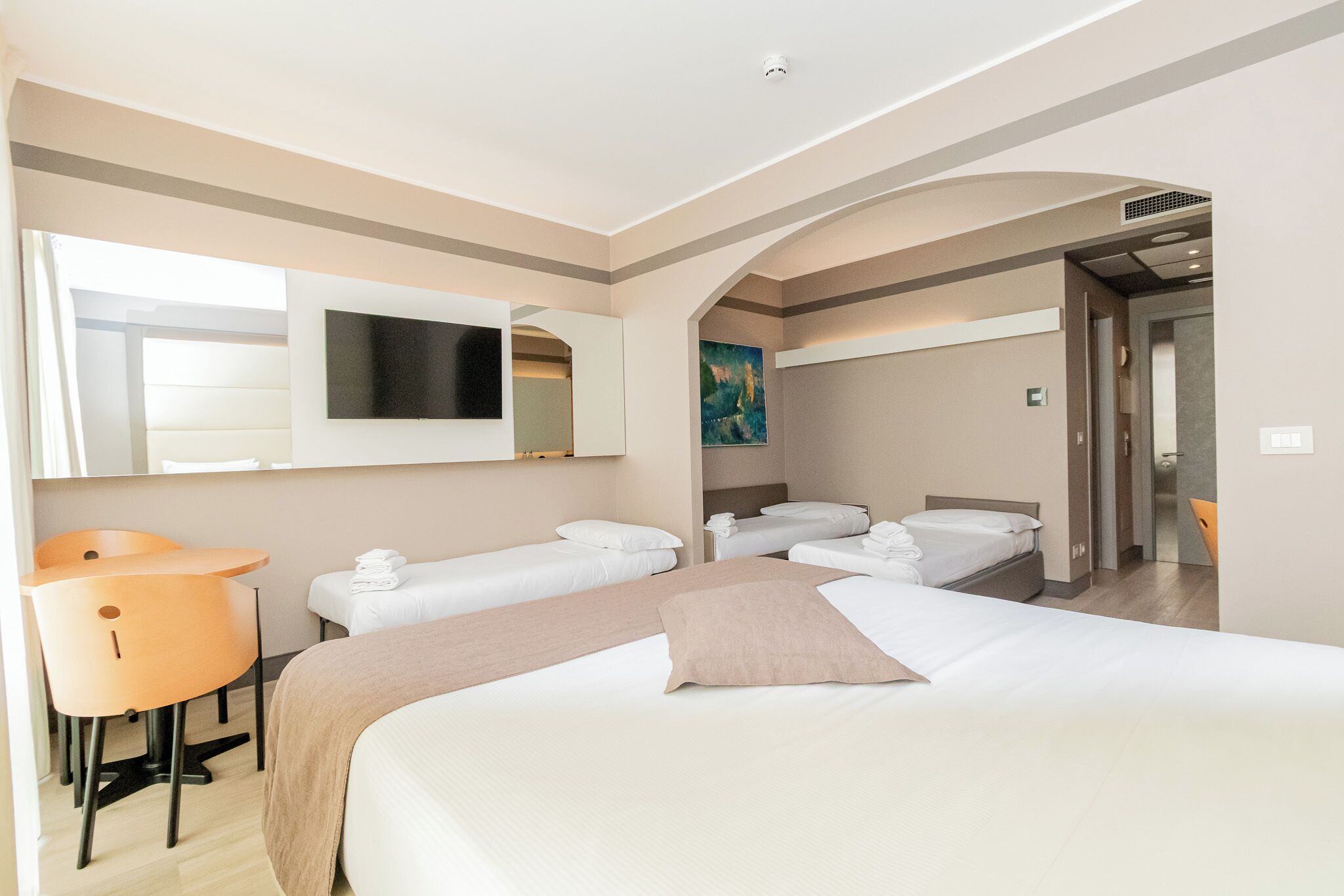 Una camera d'albergo con un letto grande, due letti più piccoli, una scrivania e una sedia.