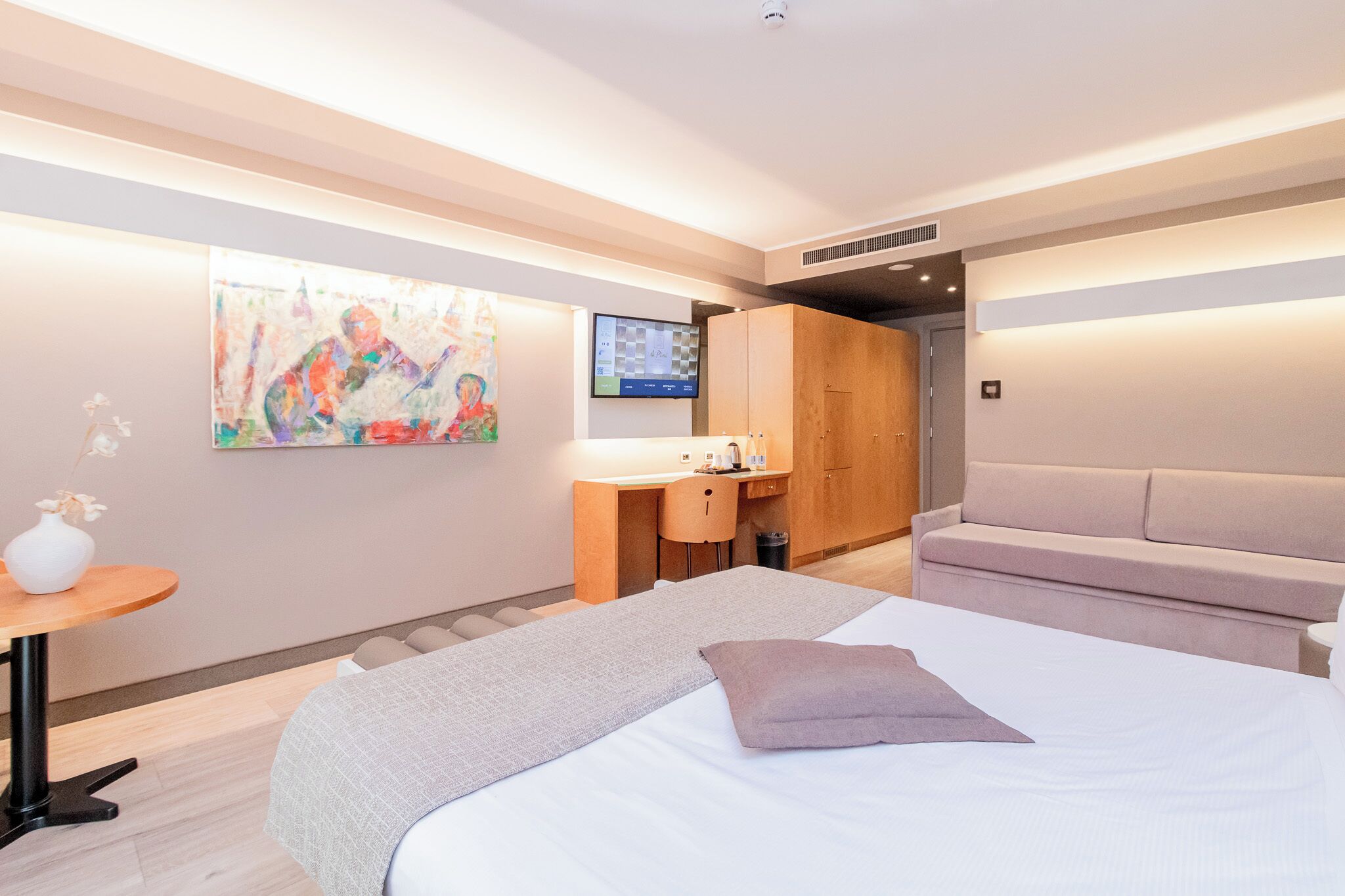 Une chambre d’hôtel moderne, équipée d’un lit, d’un bureau, d’un canapé et d’un tableau au mur.