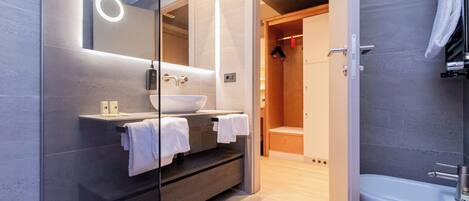 A modern bathroom with a glass-enclosed vanity, a white sink, and a bathtub.