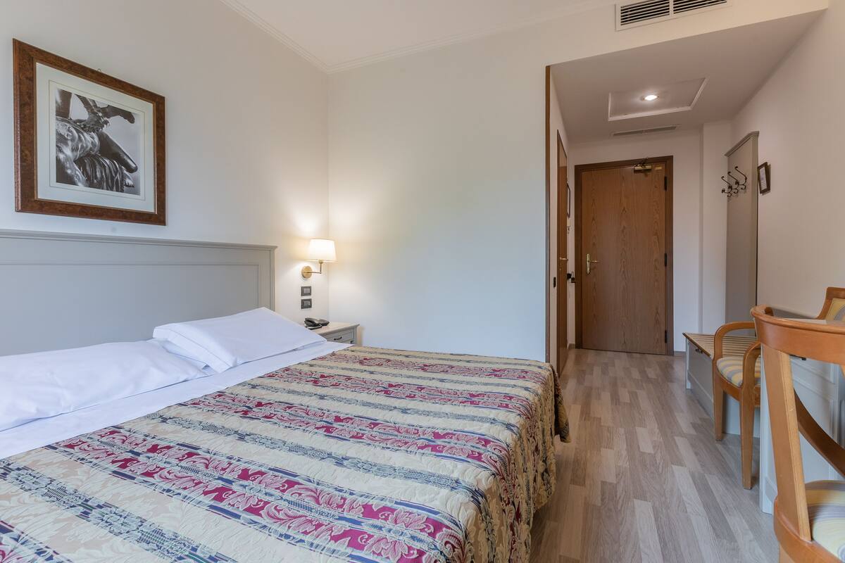 A hotel room with a bed, bedside table, lamp, and a framed picture on the wall.