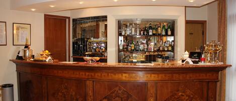 Una zona de bar con mostrador de madera, estantes con botellas y un cubo de basura.