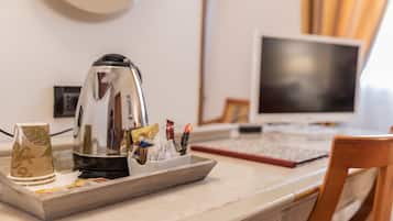 Una encimera de cocina con un hervidor, una bandeja con tazas de café y aperitivos, una computadora y una silla.